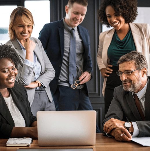 Business people gathered around a table looking at something on a notebook computer.